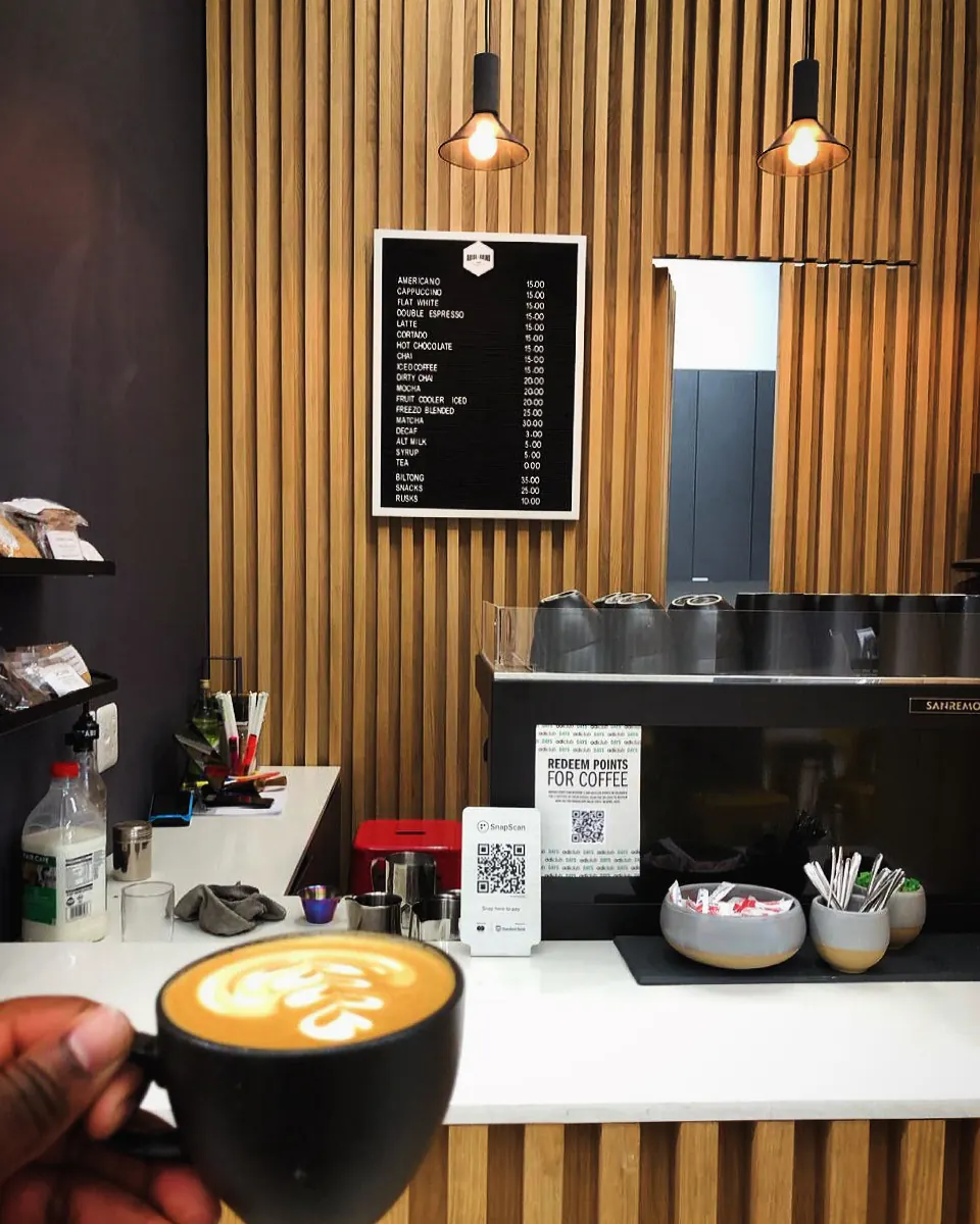 A hand holding a black cup of freshly poured Arise & Grind coffee